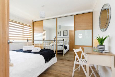 Modern bedroom in a cosy beach bolthole in Bracklesham Bay, featuring a comfortable bed, mirrored wardrobe, and minimalist decor.